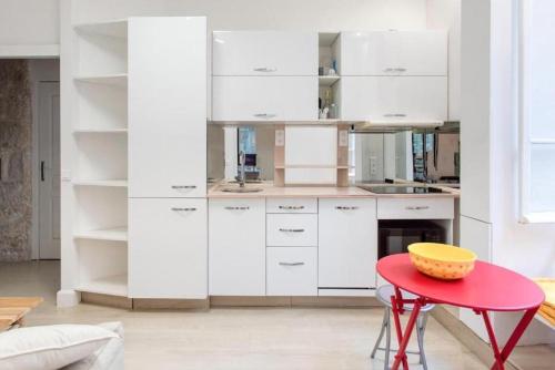 une cuisine avec des placards blancs et une table rouge dans l'établissement ROSIE-Charmant Cocon à Beausoleil, aux Portes de Monaco, à Beausoleil