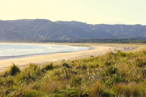 una spiaggia sabbiosa con montagne sullo sfondo di Sunset Haven - Mahia Holiday Home a Mahia