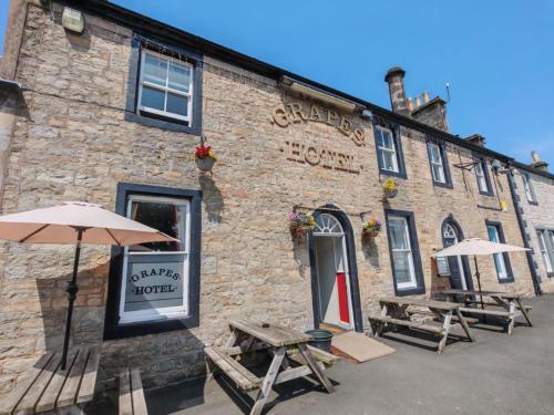 a brick building with two picnic tables and umbrellas at The Grapes Hotel in Newcastleton