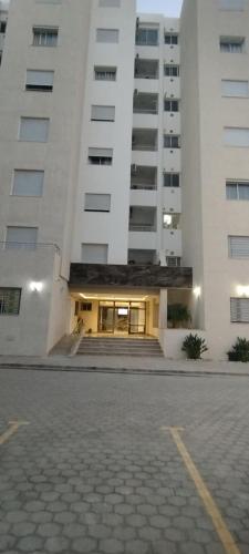 a large white building with a parking lot in front of it at ConfortTek apartment in Boumhel El Bassatine