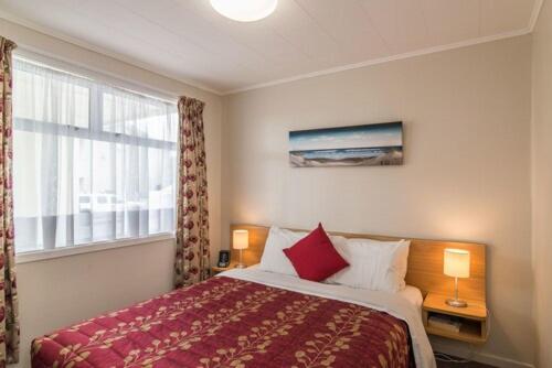 a bedroom with a bed with a red blanket and a window at Avana Suites in Lower Hutt