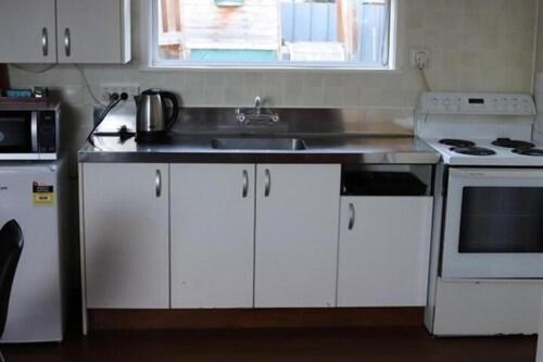a kitchen with white cabinets and a sink and a microwave at Avana Suites in Lower Hutt