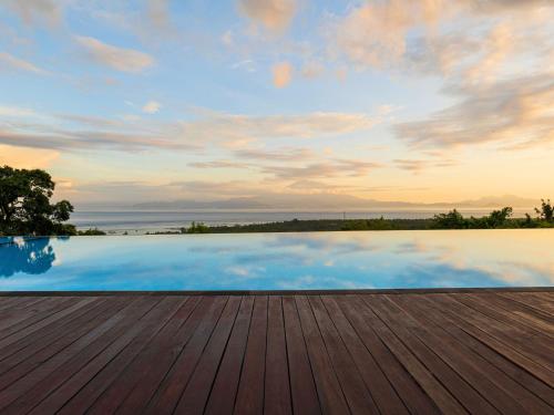 a pool with a wooden deck and a cloudy sky at Semabu Hills Hotel Nusa Penida in Nusa Penida