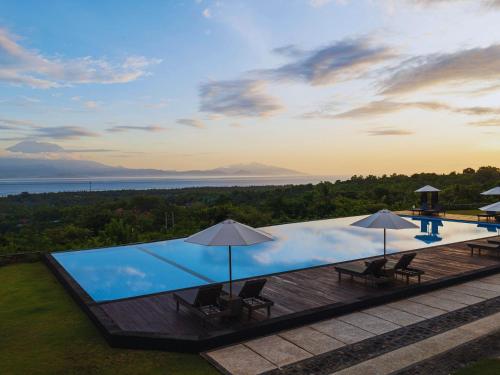 an infinity pool with chairs and umbrellas on a deck at Semabu Hills Hotel Nusa Penida in Nusa Penida