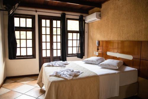 a bedroom with a bed with white sheets and windows at Lonier Ilha Inn Flats in Abraão