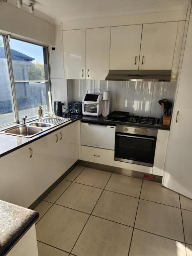 a kitchen with white cabinets and a sink and a microwave at Canal Condo in Mooloolaba