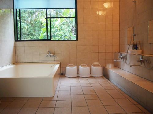 baño con 2 aseos, bañera y ventana en Yakushima Pension Ichigoichie, en Yakushima