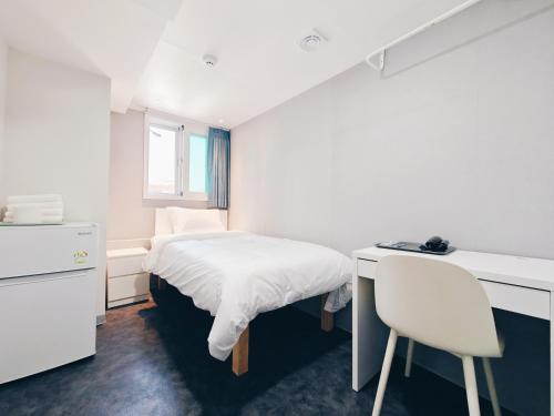 首尔W hostel的一间白色的小卧室,配有一张床和一张书桌