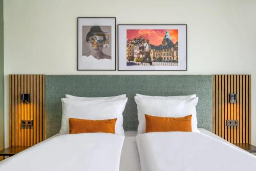two beds in a hotel room with pictures on the wall at Aspire Palais Recklinghausen, Trademark Collection by Wyndham in Recklinghausen