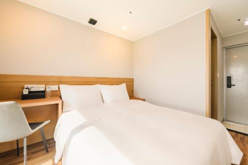 a bedroom with a white bed and a desk and a chair at Hotel Moon in Jeju