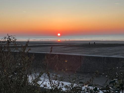 a sunset at the beach with people walking on the beach at Pavillon d'Éole in Berck-sur-Mer