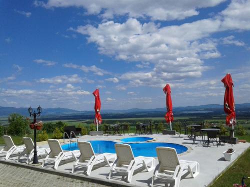 a pool with white chairs and tables and red umbrellas at Gledkata Complex in Skobelevo