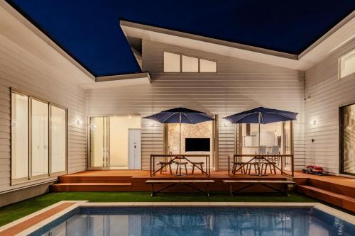 a house with two tables and two umbrellas at Play Stay 一宮 サウナ BBQ 広々ガーデン in Ichinomiya