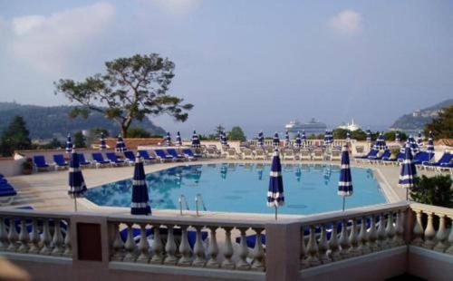 - une piscine avec des parasols et des chaises bleus et blancs dans l'établissement Rez de jardin privatif à 150m de la mer, à Villefranche-sur-Mer