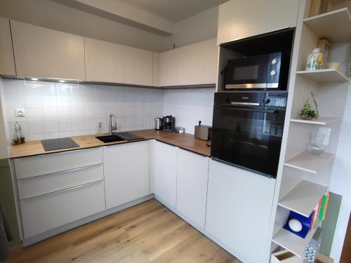 une cuisine avec des armoires blanches et un réfrigérateur noir dans l'établissement Appartement cosy avec Jardin clôturé, à Bretenoux