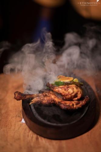 two pieces of meat cooking on a grill with smoke at Ethnotel, Kolkata Airport in Kolkata