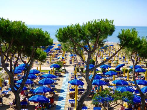 a beach with blue umbrellas and people sitting on the beach at Mon Repos in Lido di Jesolo