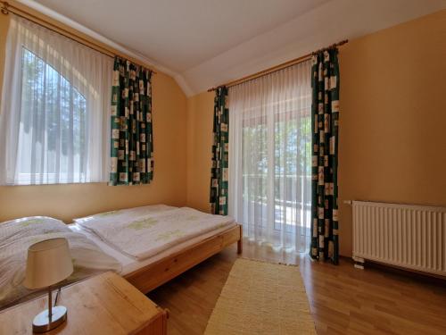 a bedroom with a bed and two large windows at Sunshine Beach House, DIREKT AM SEE, eigenes BOOT, PRIVATE BEACH, Grill, WLAN in Szántód