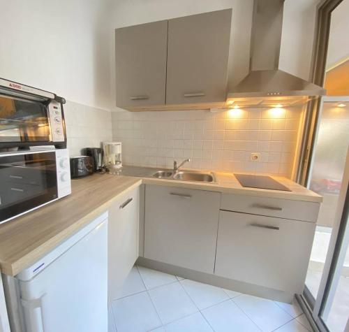 une cuisine avec des armoires blanches et un évier dans l'établissement Cannes proche Croisette - Studio balcon vue sur jardin, à Cannes