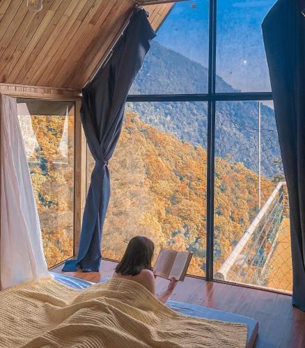 a woman laying in bed reading a book in front of a window at An House, Farm & Trekking in Tam Ðảo