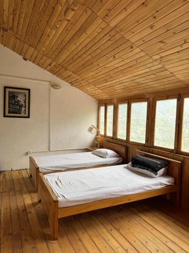 two beds in a room with wooden ceilings and windows at The Walnut Tree Lodge, Naltar in Jugut
