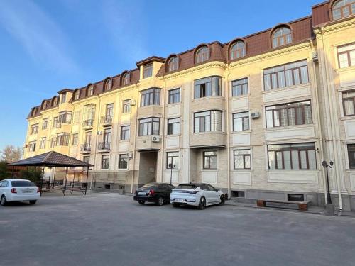 un gran edificio con dos coches estacionados en un estacionamiento en Central Nest Samarkand, en Samarkand