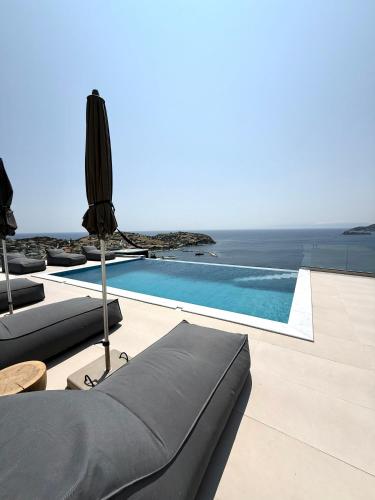 a swimming pool with chaise lounges next to the ocean at PETRA Luxury Villas in Áyioi Apóstoloi