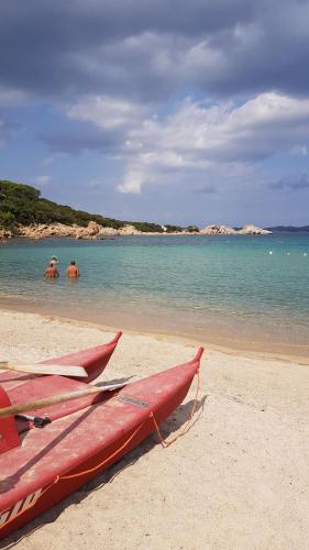 a red surfboard on a beach with people in the water at La casa dei tramonti in Baja Sardinia