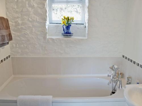 ein Badezimmer mit einer weißen Badewanne und einer Vase mit Blumen. in der Unterkunft Yarde cottage rural Devon Dog friendly in Membury