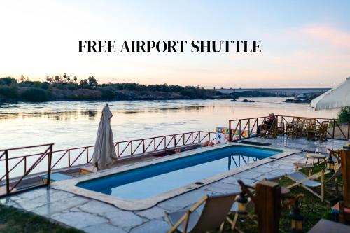 a swimming pool next to a river with the words free airport shuttle at Fenti Nubian Resort in Aswan