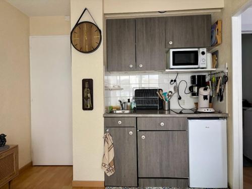 une cuisine avec des armoires en bois et une horloge au mur dans l'établissement Appartement vue latérale mer proche marché Arago, à Les Sables-dʼOlonne