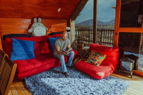 a man sitting on a red couch in a living room at La Cabaña Alpina de Huimilpan in Pedro Escobedo