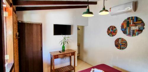 a living room with a table and a tv on the wall at Portal Suítes Casa do Lago in Paraty