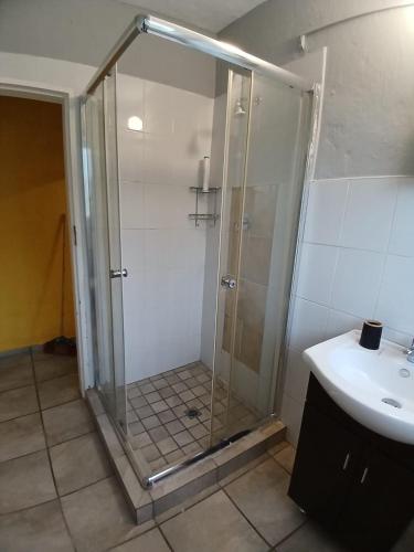 a shower with a glass door next to a sink at Cottage in Kloofendal in Roodepoort