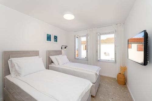 two beds in a white room with two windows at House Tre Venti with pool in Sveti Filip i Jakov