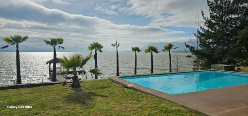 a swimming pool next to a body of water with palm trees at Casa Lago Rapel in Las Cabras