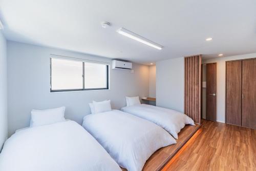 zwei Betten in einem Zimmer mit weißen Laken in der Unterkunft Flower Base Botan in Fukuoka