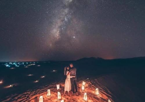 a man and a woman standing on the beach at night at Sahara horizon Camp in Merzouga