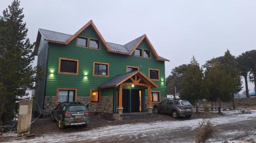 a green house with two cars parked in front of it at Los Basaltos departamentos in Caviahue