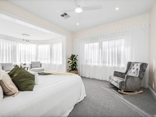 a white bedroom with a large bed and a chair at Coastal Dream BeachFront Oasis in Newcastle