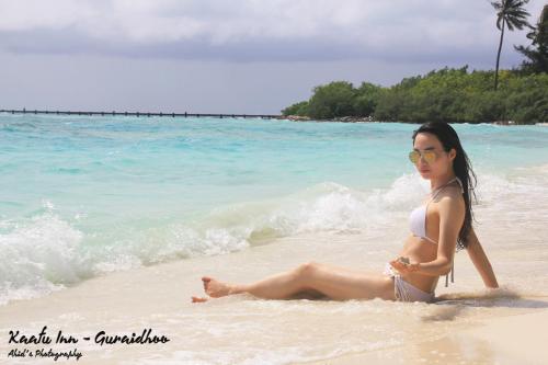 a woman in a bikini sitting on the beach at Kaafu Inn Guraidhoo in Guraidhoo