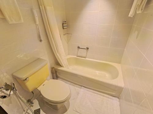 a white bathroom with a toilet and a bath tub at City Garden Hotel Makati in Manila