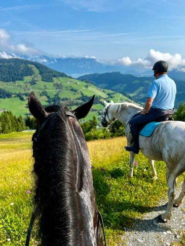 two men riding horses on a grassy hill at Hotel Der Wastlhof - Pools, Spa & eigene Reitschule in Niederau