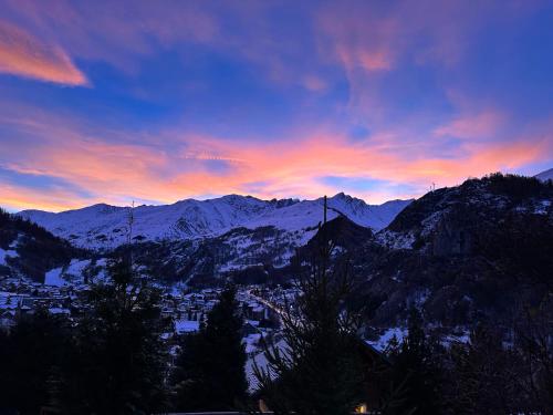 a sunset over a snowy mountain range with a city at Hôtel-Chalet les Mélèzes in Valloire