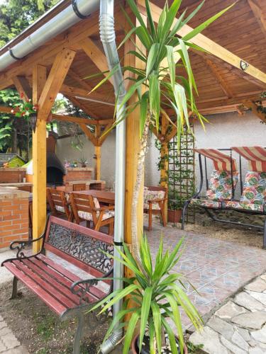 a bench under a wooden pergola with a palm tree at Liget Nyaralóház és Apartman Liget in Szilvásvárad