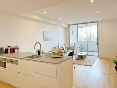 a kitchen with a sink and a living room at Chic 1BR Condo next to Croydon Station in Sydney