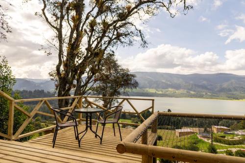 a deck with two chairs and a table and a view of a lake at Neusa Hills Glamping in Tausa Viejo