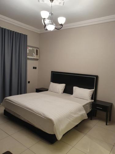 a bedroom with a bed with white sheets and a chandelier at ابراج الراحة بلازا شركة راحتي للشقق المخدومه in Taif