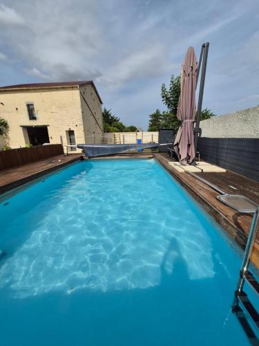 une grande piscine bleue avec un parasol dans l'établissement maison de bourg au calme, proche du Futuroscope, à Yversay