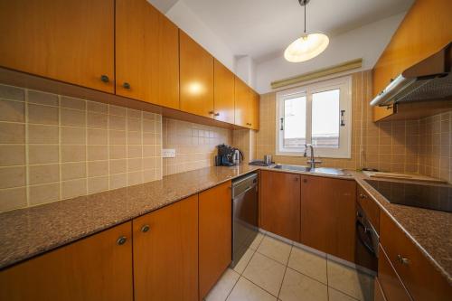 a kitchen with wooden cabinets and a sink and a window at Seaside Villa Luci with jacuzzi and just minutes away from Ayia Triada beach in Paralimni